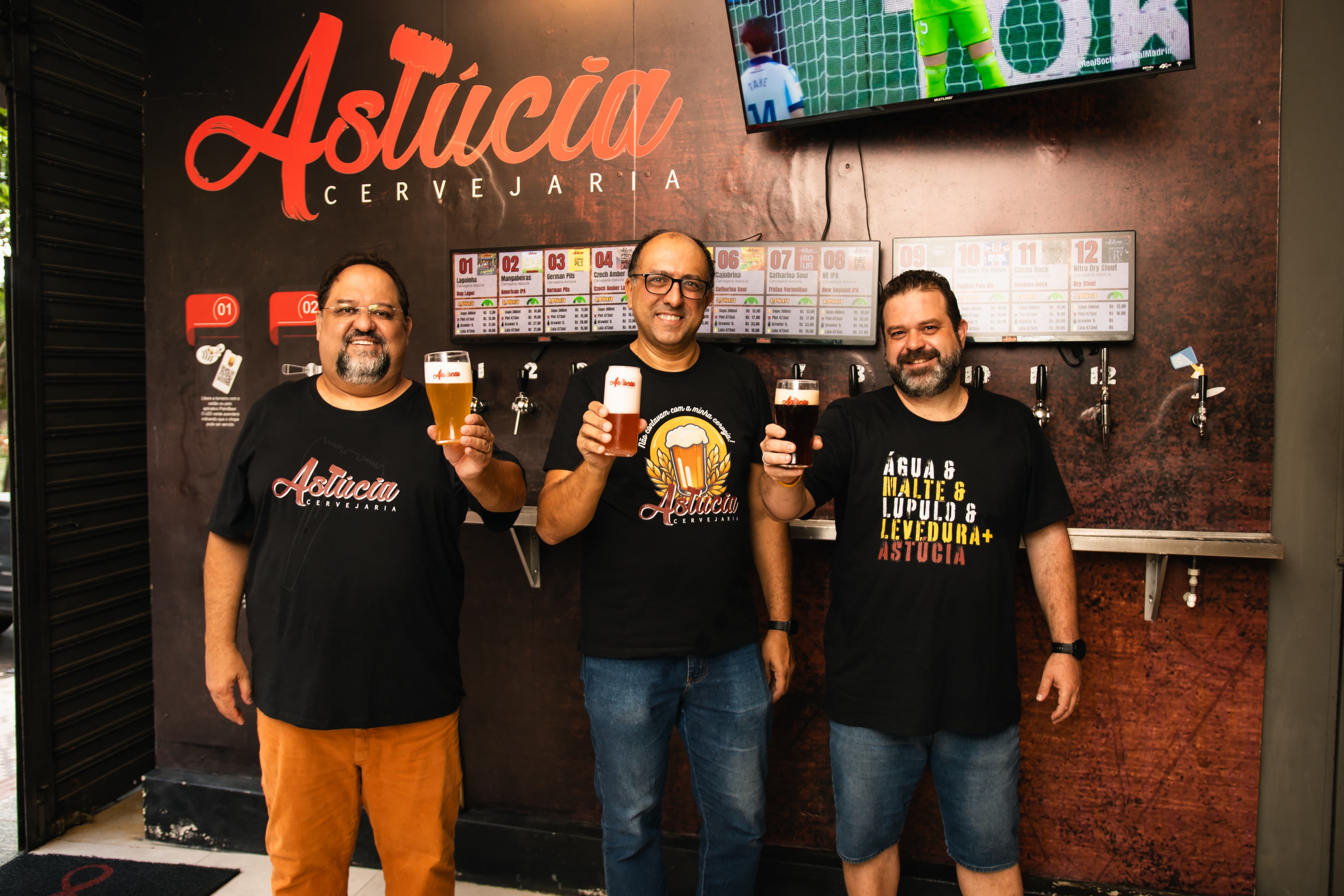 Equipe da Astúcia no taproom com cervejas na parede de taps